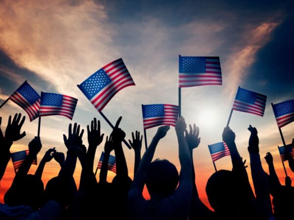 crowd silhouette waving American flags at sunset